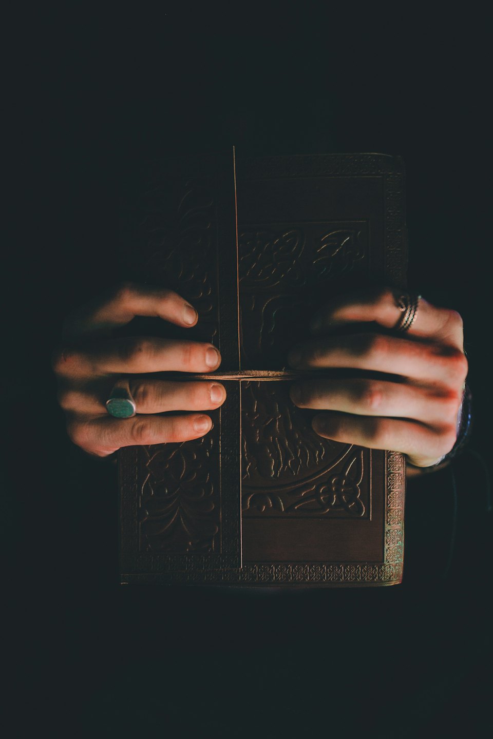 Hands opening an ornate, antique book with embossed patterns.