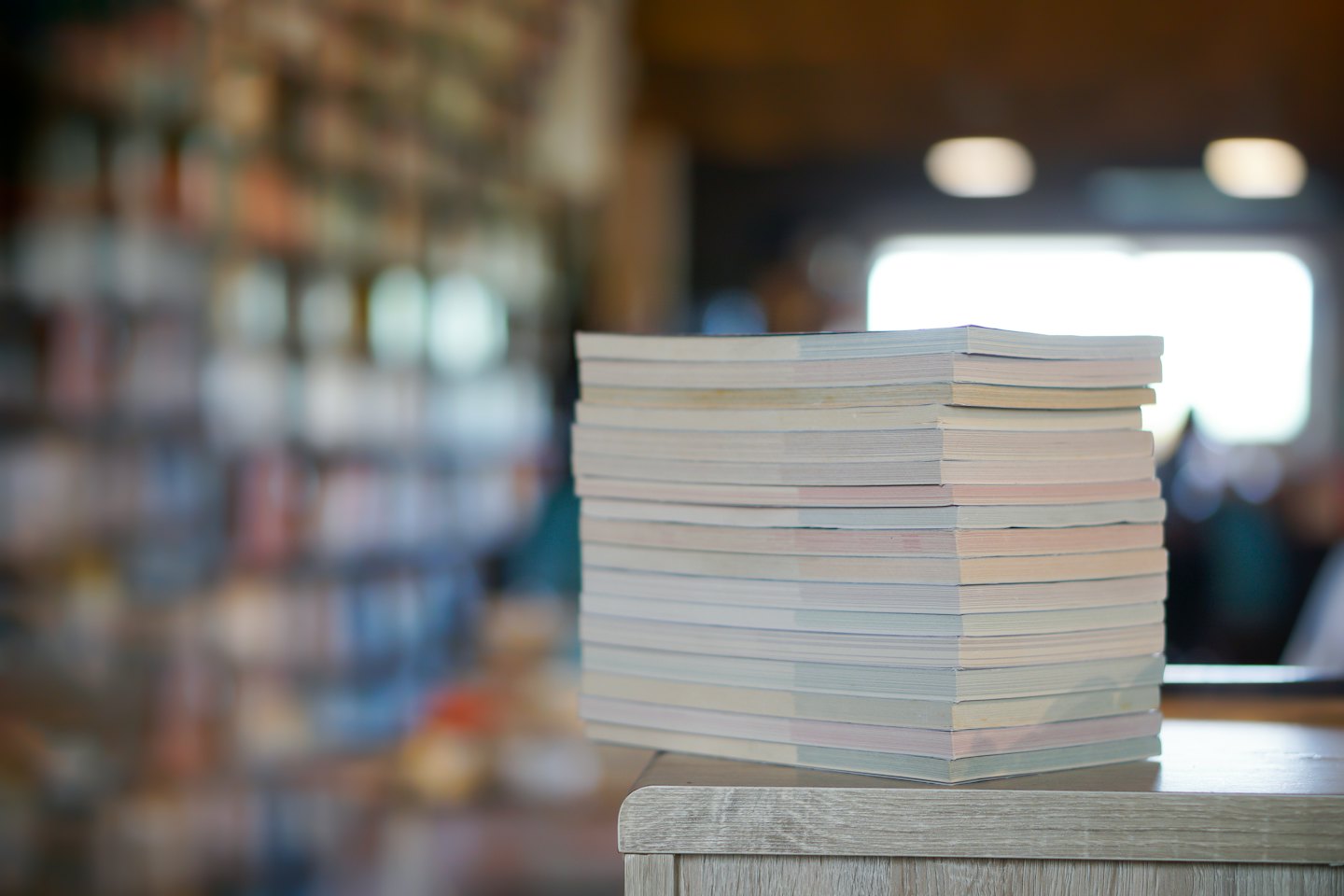 A stack of thin books rests on a wooden table.
