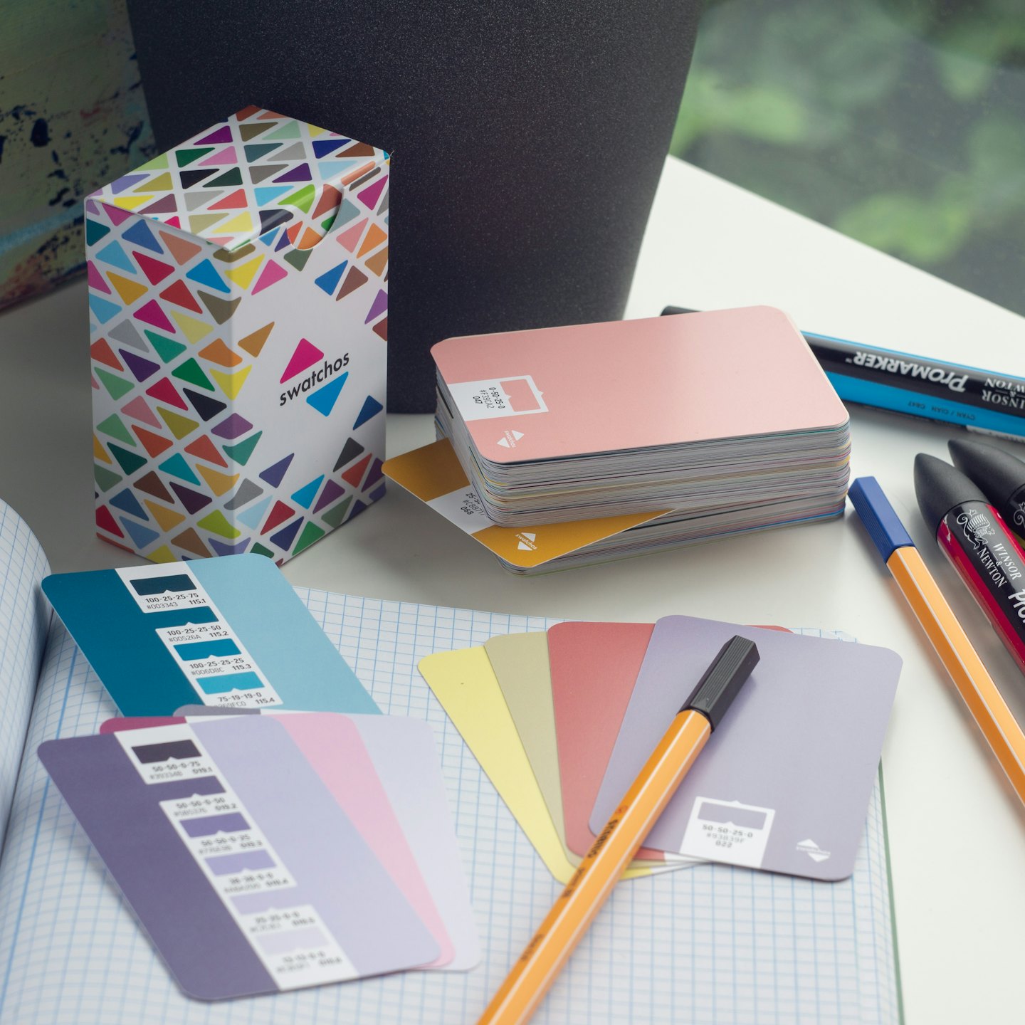 Color swatches and art markers on a white desk with a notebook.